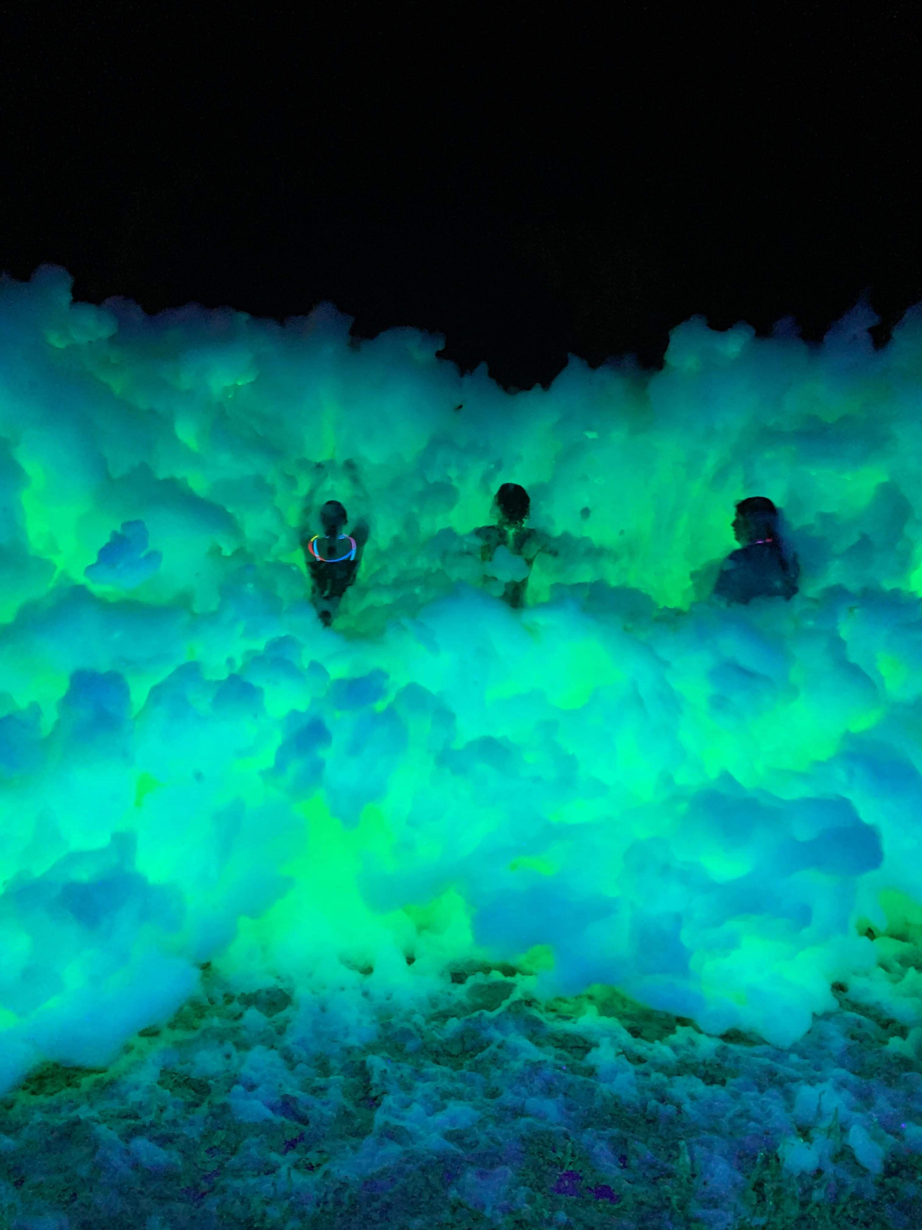 Guests playing in glowing green foam at a nighttime party