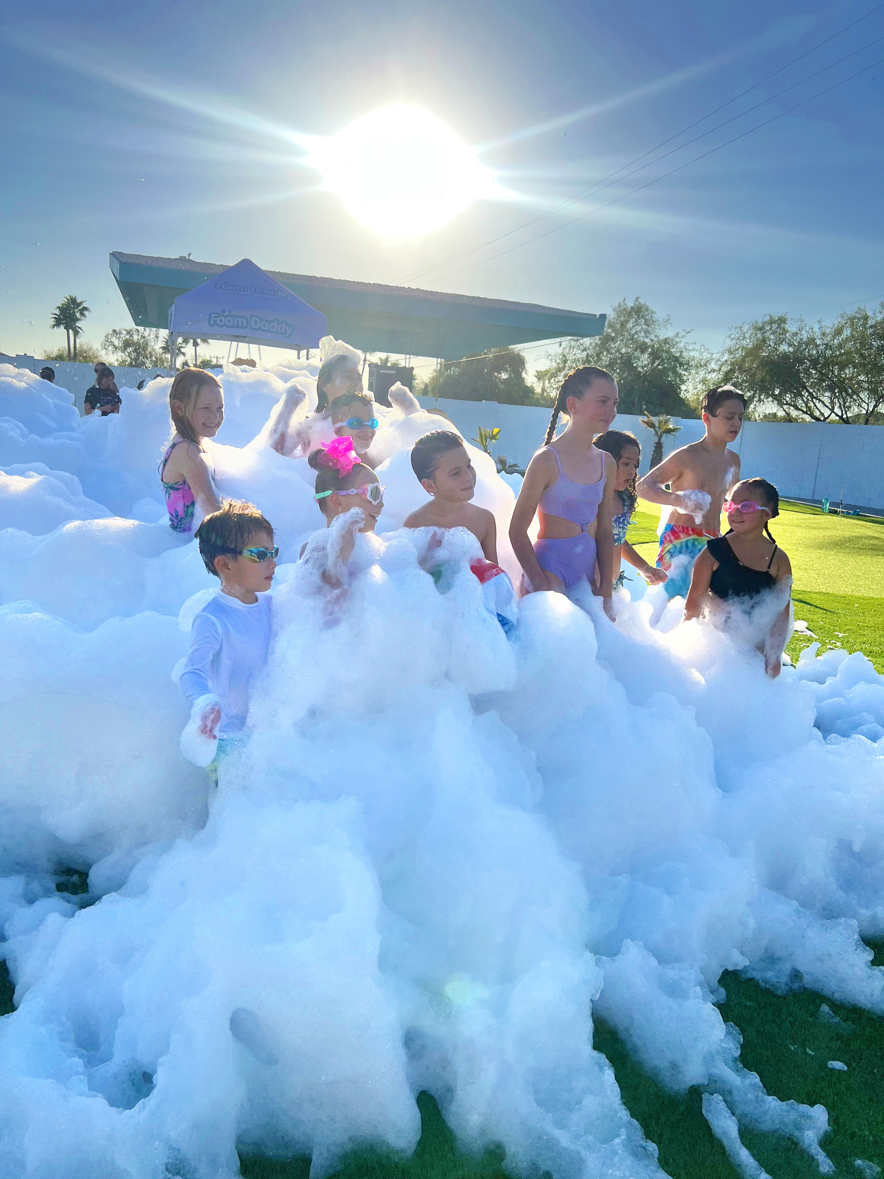 A group of children gathered in foam under the afternoon sun